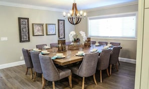 A dining room with a wooden table, grey upholstered chairs, and a chandelier. - Designer decorated 6 bedroom pool house (Santa Ana)