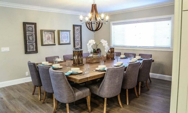 A dining room with a wooden table, grey upholstered chairs, and a chandelier.