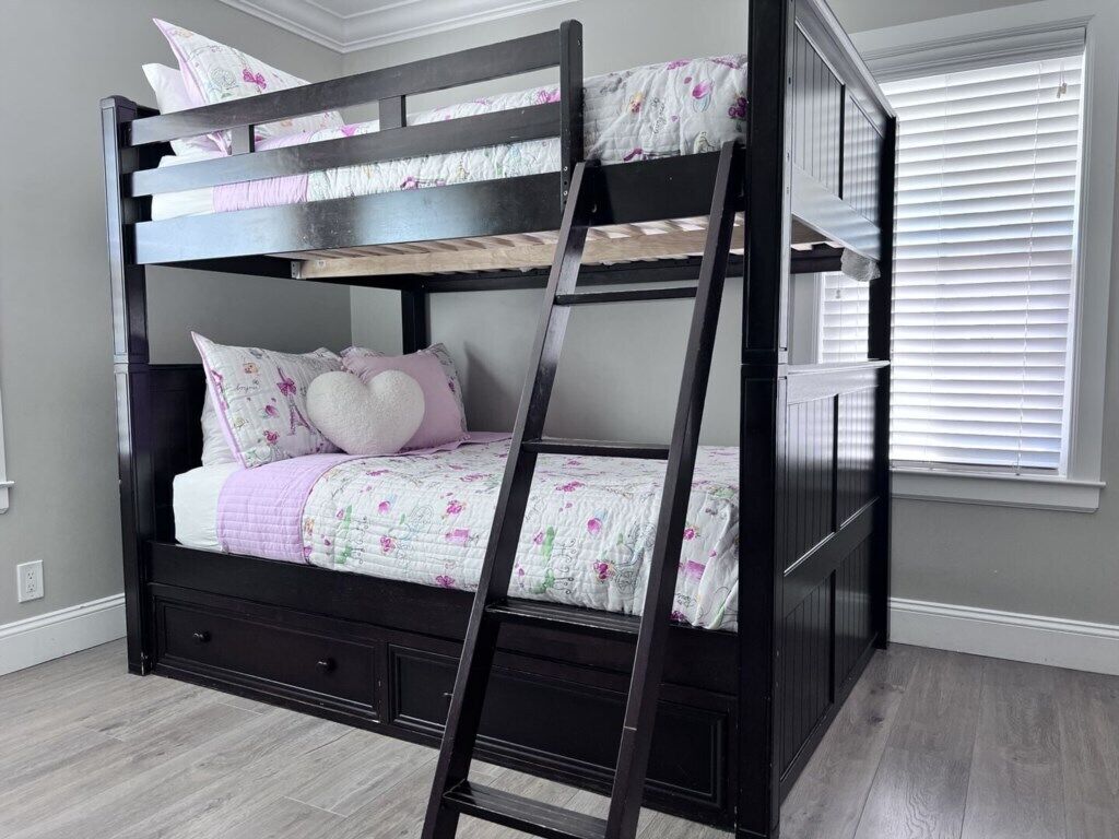 A bunk bed with a ladder, a drawer, and a window with blinds.
