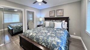Une chambre à coucher avec un lit, un ventilateur de plafond, une table de chevet, un miroir et une fenêtre.