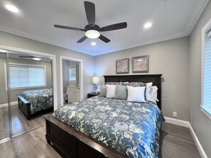 A bedroom with a bed, a ceiling fan, a nightstand, a mirror, and a window.