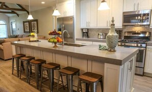 A kitchen with a central island, bar stools, stainless steel appliances, and a vase. - Designer decorated 6 bedroom pool house (Santa Ana)