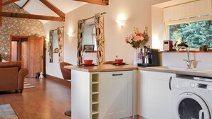 Cocina compacta con lavadora, cafetera y comedor con sofá y mesa.