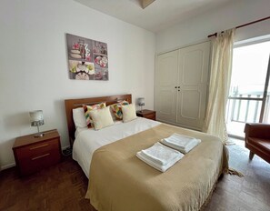 A hotel room with a bed, a wardrobe, a nightstand, a lamp, and a window with curtains. - Yvonne Beach Apartment by Refugio (Almada)