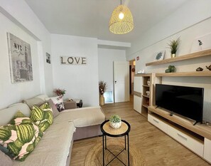 A modern living room with a sofa, a television, and decorative items. - Yvonne Beach Apartment by Refugio (Almada)