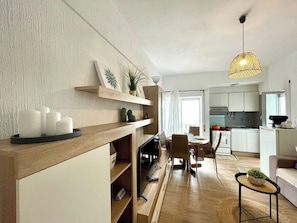 A modern living room with a flat-screen TV, wooden shelving, and a dining area with a table and chairs.