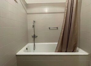 Un bagno standard rivestito di piastrelle bianche, con una vasca, una doccetta e un portaservizi.