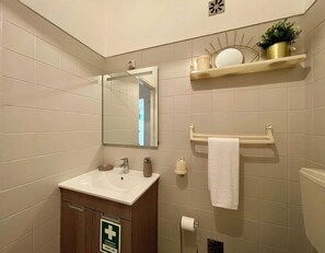 Une salle de bain équipée d’un lavabo, d’un miroir, d’un porte-serviettes et d’un panneau indiquant la présence d’une trousse de premiers secours.