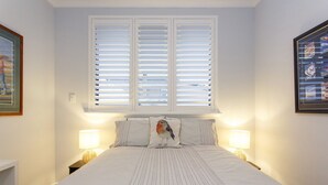 Una cama bien hecha con colcha a rayas, dos lámparas de noche y una ventana con persianas.