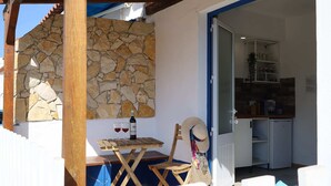 A covered outdoor area with a stone wall, a wooden table with glasses and a bottle, and a chair. - Lizandro´s  Pé  n' Areia (Mafra)