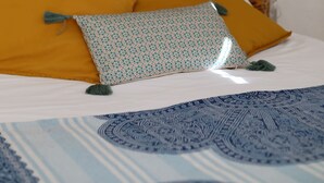 A bed with a wooden headboard, multiple pillows, and a patterned bedspread. - Lizandro´s  Pé  n' Areia (Mafra)