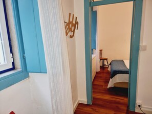 Ein schmaler Flur mit Holzboden, der zu einem Zimmer mit Bett und Stuhl führt.