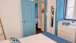 Um quarto com uma cama, cômoda, espelho e porta que dá para outro espaço.