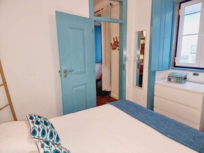 Una camera da letto con un letto, una cassettiera, uno specchio e una porta che dà su un'altra stanza.