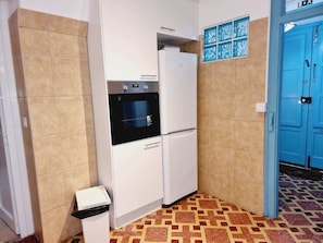 Eine kleine Küche mit Backofen und Kühlschrank, einem Mülleimer und einem gemusterten Boden.