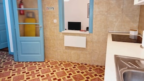 Uma cozinha com porta azul, painel de azulejos, bancada branca e chão estampado.