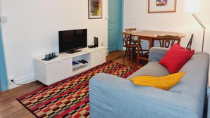 Uma sala de estar com televisão, mesa de jantar e sofá.