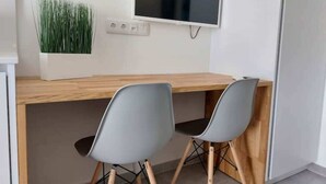 Un espace de travail moderne avec un bureau en bois, deux chaises grises, un téléviseur à écran plat et une plante en pot.