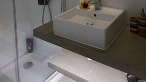 A modern bathroom with a glass shower enclosure, a white sink with a single flower, and a large mirror above the sink. - Mocho's  - Apartment (Mafra)