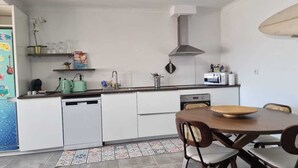 Una cocina funcional con lavavajillas, microondas y estufa. Hay una mesa de comedor con sillas y un florero decorativo en la encimera.