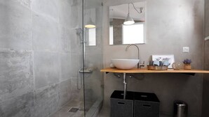 Un baño moderno con cabina de ducha de vidrio, un lavabo sobre encimera y un mueble de tocador de madera.