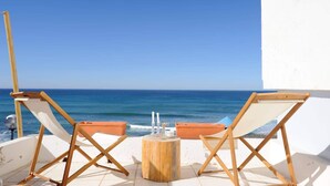 Una terraza frente al mar con dos sillones de madera, una mesita redonda y vistas al oc éano.