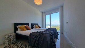 Un dormitorio con dos camas, un reposapiés estampado y vistas al mar.