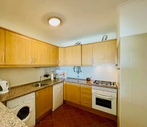 Une cuisine compacte avec des meubles en bois, un lave-vaisselle encastré, une cuisinière et un lave-linge.