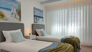 Hotellihuone, jossa on kaksi sänkyä, yöpöytä ja maalaus, jossa on kuvattuna rantamaisema.
