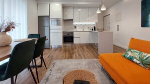 Moderni keittiö, jossa on valkoiset kaapit, sisäänrakennettu uuni sekä ruokailutila, jossa on pöytä ja tuolit.