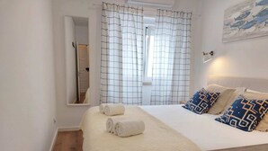 A hotel room with a bed, a bedside table, a mirror, and a window with curtains. - Ericeira - Parrot`s House (Mafra)