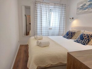 Una camera d'albergo con un letto, un comodino, uno specchio e una finestra con tende.