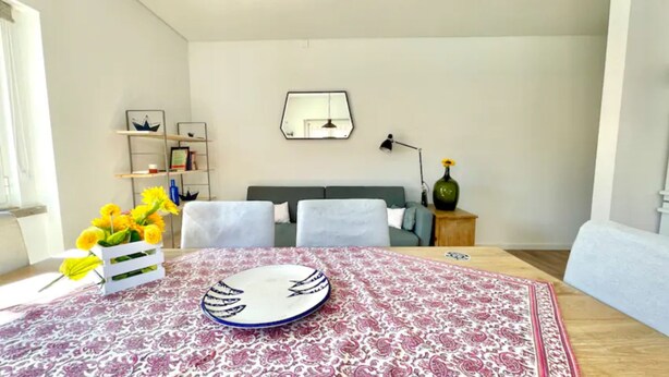 A living room with a dining table, sofa, and a decorative mirror on the wall. - Ericeira - Parrot`s House (Mafra)