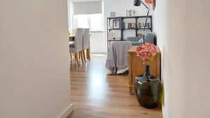 A modern living room with a dining area, a bookshelf, and a vase with flowers. - Ericeira - Parrot`s House (Mafra)