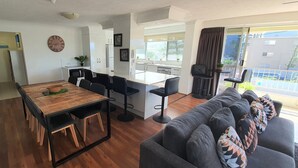 Ein moderner Wohnraum mit einem Holzespeisetisch, schwarzen Barhocker, einem grauen Sofa und einer Küche mit weißen Schränken.