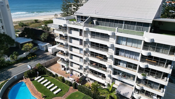 Ein mehrstöckiges Hotel mit Balkonen, einem Schwimmbad und Blick auf den Strand.