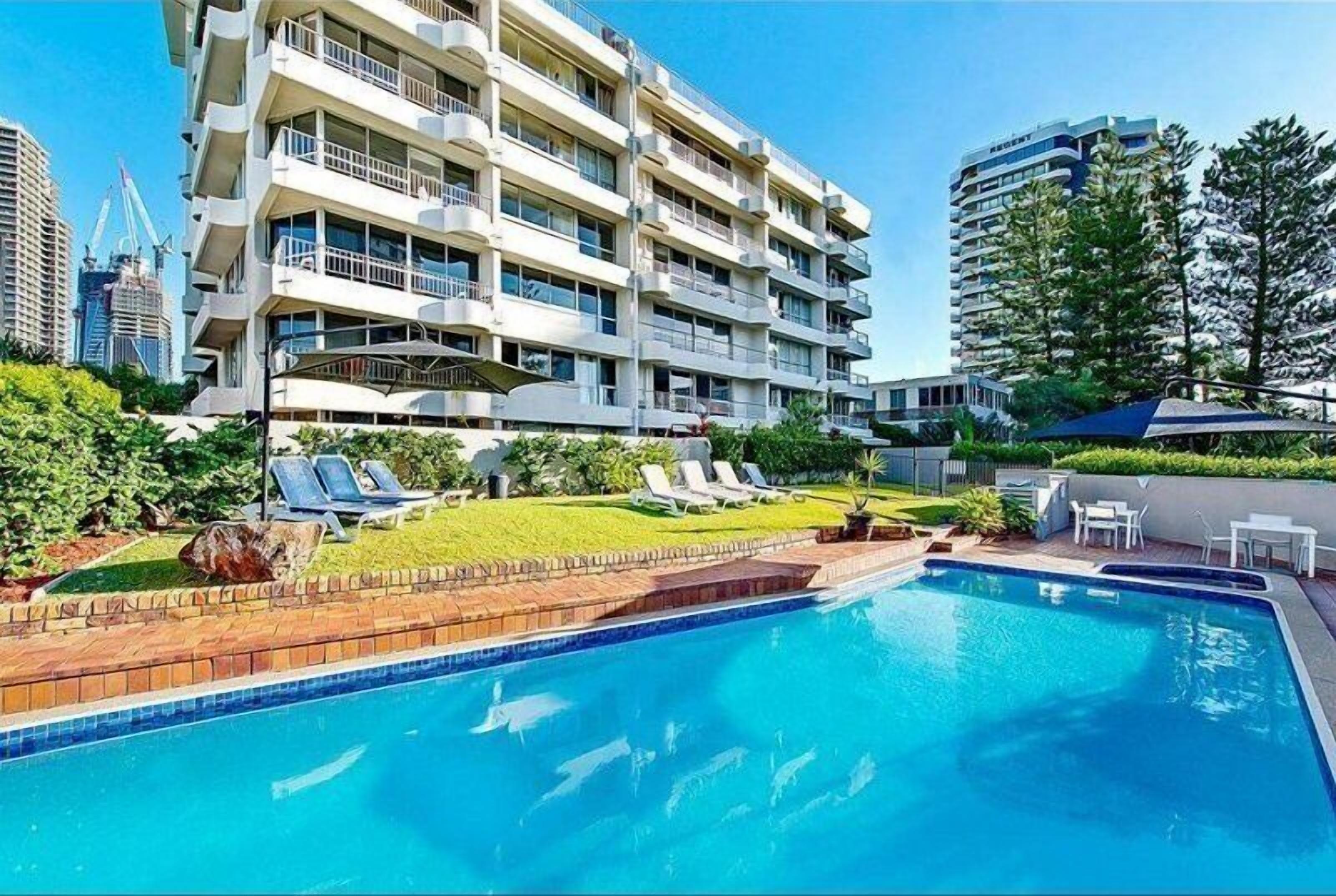 A modern hotel with a swimming pool, multiple balconies, and a well-maintained garden.