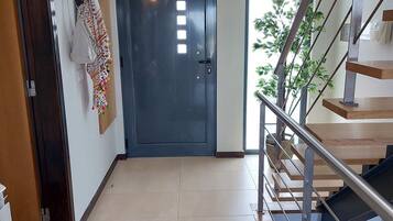 A hallway with a dark door, a staircase with metal railings, and a plant near the door.