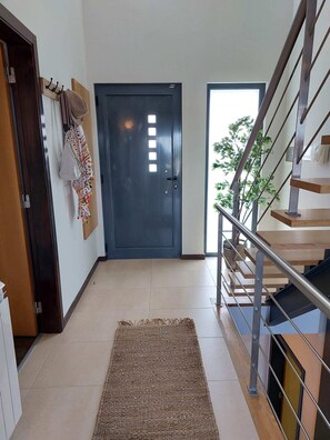 Un pasillo con una puerta oscura, una escalera con barandillas metálicas y una planta cerca de la puerta.
