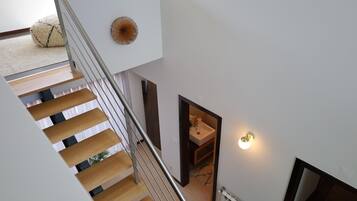 A modern interior with a staircase leading to a second floor, a small bathroom with a sink, and a decorative wall piece.