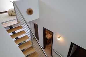 Un interior moderno con una escalera que conduce a un segundo piso, un baño pequeño con un lavabo y un elemento decorativo en la pared.