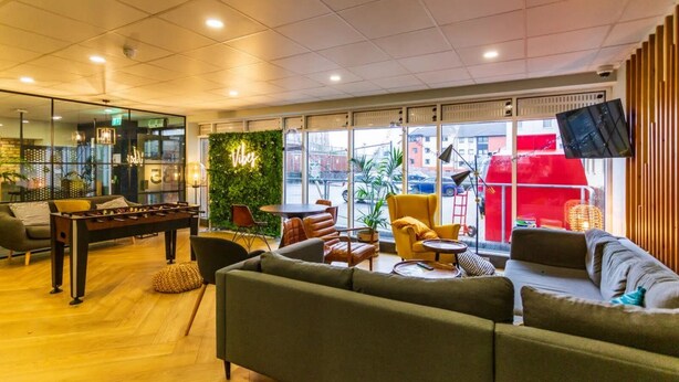A modern lounge area with a foosball table, comfortable seating, and large windows offering city views. - Student Only Buchanan View (Glasgow)