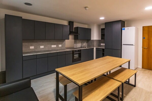 Een moderne keuken met donkere kastjes, een houten tafel en een witte koelkast.