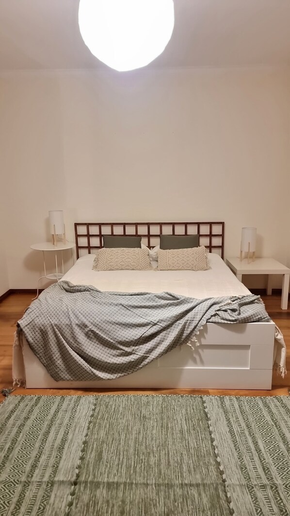 Un dormitorio con una cama, dos mesitas de noche, una lámpara de techo redonda y una alfombra estampada.