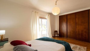 Quarto com cama, cadeira, guarda-roupa e luminária suspensa.
