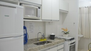Una cocina compacta con armarios blancos, un microondas, un fregadero y una estufa.