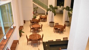 Amplio espacio interior con varias mesas y sillas de madera, plantas en macetas y una escalera.