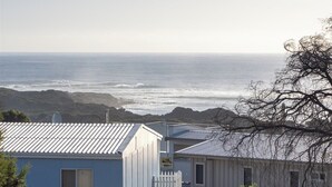 Vista costeira com duas cabanas azuis, uma delas com varanda branca, e uma árvore em primeiro plano.