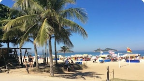 A beach with palm trees, umbrellas, and people. - PEPÊ BEACH APARTMENT  (Barra da Tijuca Rio de Janeiro)
