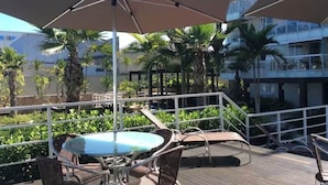 A deck with outdoor seating, including a table and chairs, and large umbrellas providing shade. - PEPÊ BEACH APARTMENT  (Barra da Tijuca Rio de Janeiro)
